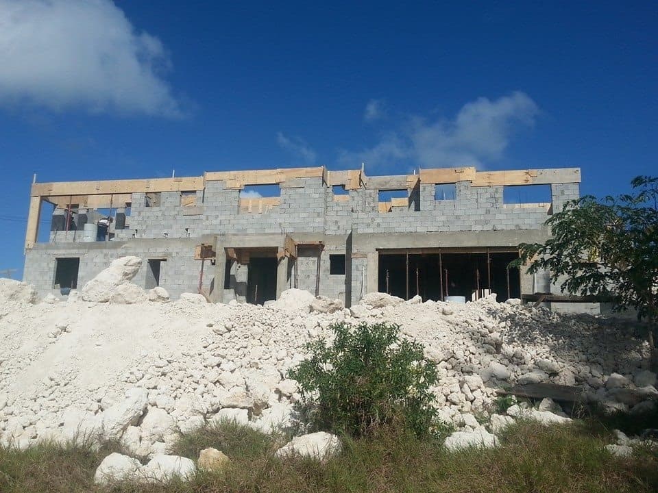 Two-storey block structural shell with roof framing beginning, building material stockpiled on site