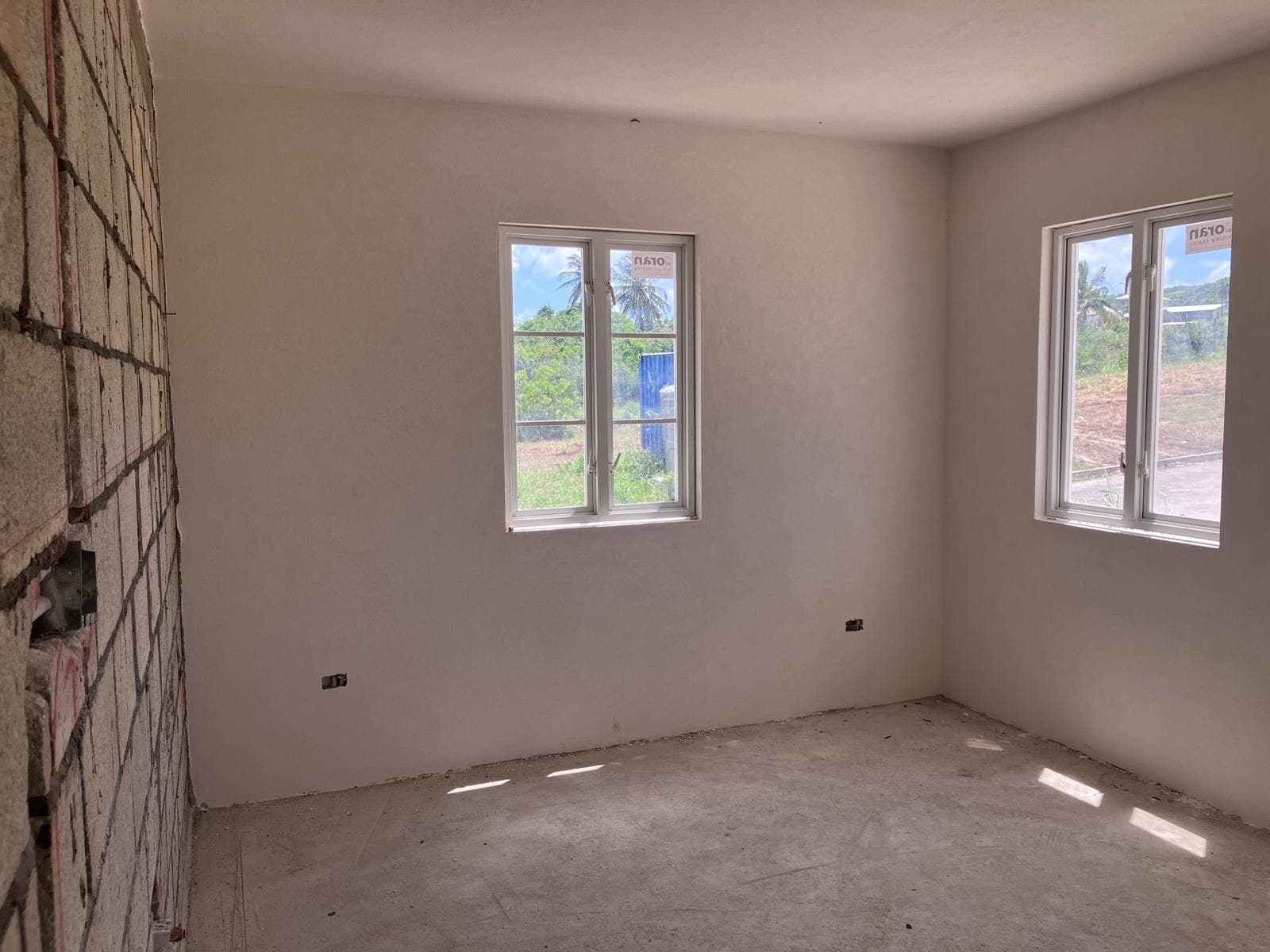 Plastered interior room with two windows overlooking the neighbouring lot