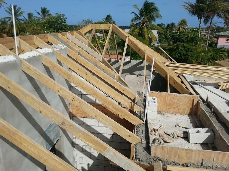 Close-up of timber roof truss framing over a block structure, palm trees in background