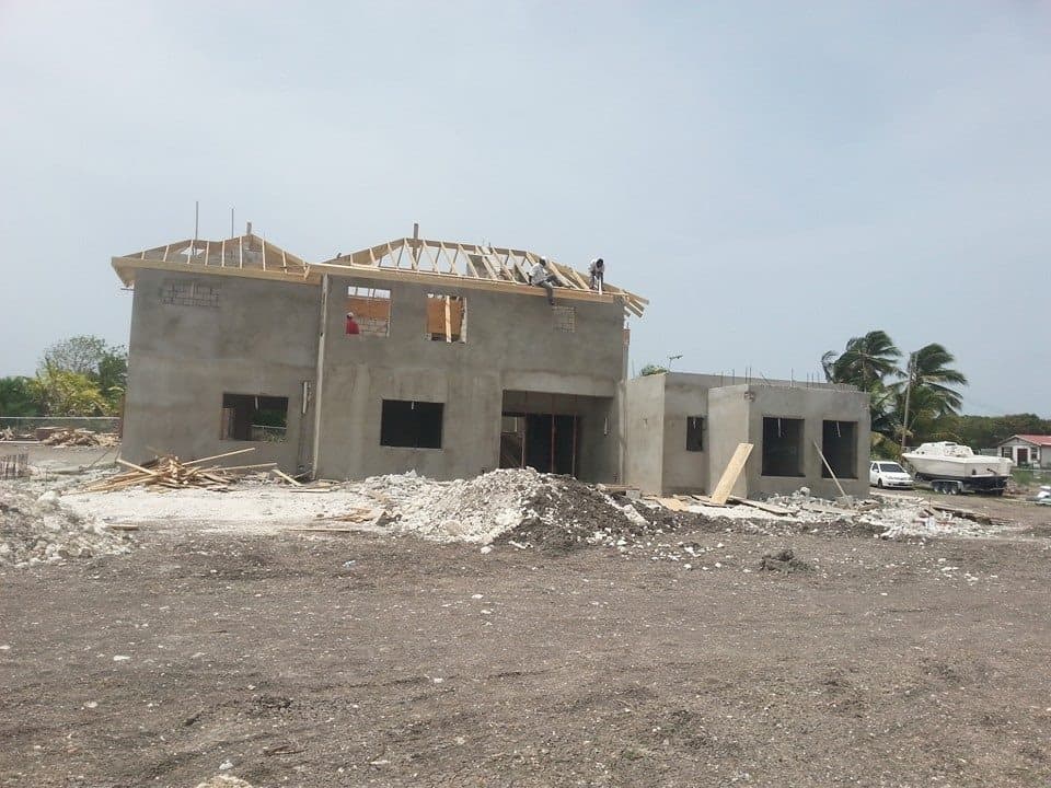 Two-storey structural shell with roof framing underway, workers visible at roofline