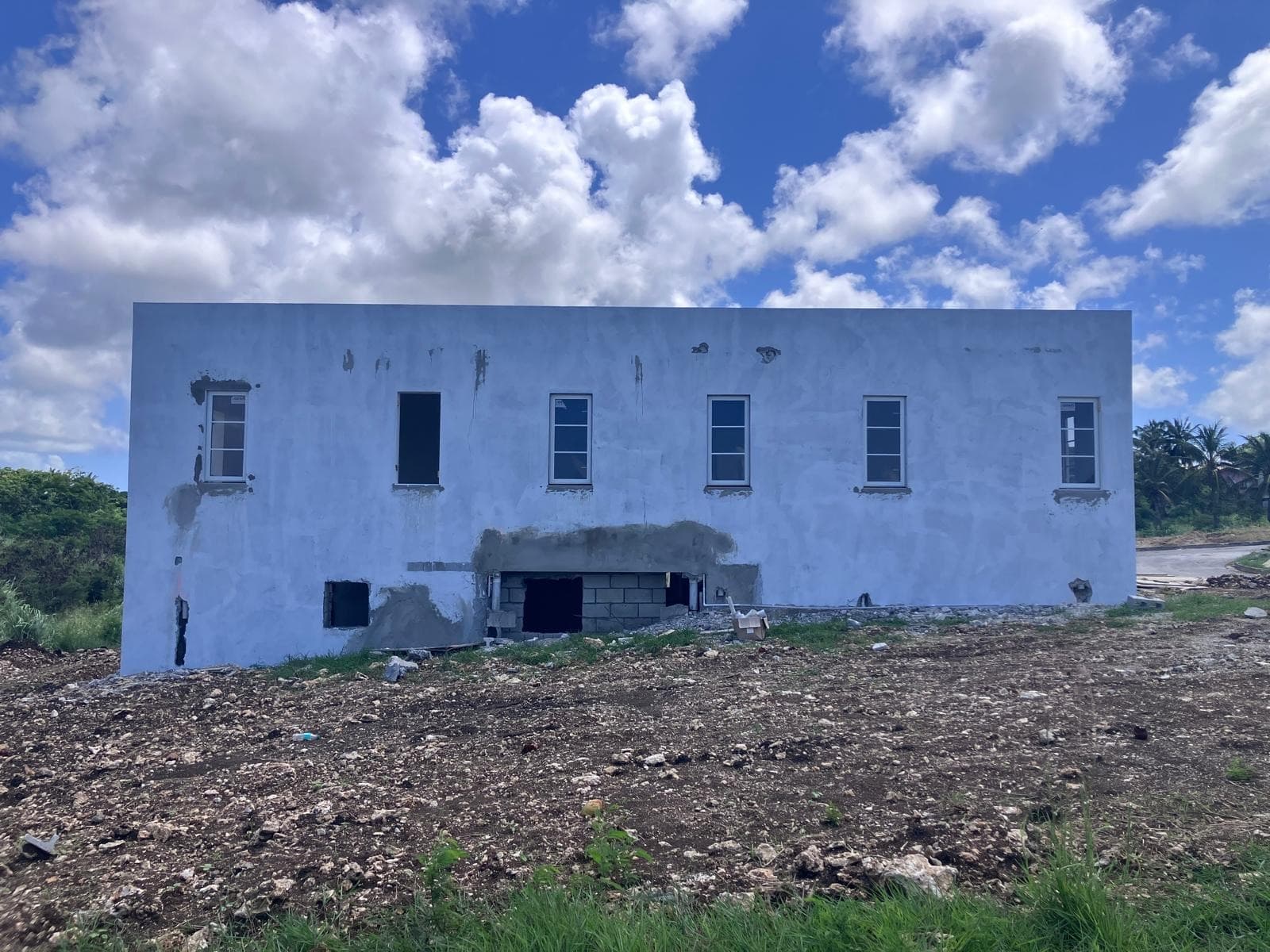 Unfinished building elevation with multiple window openings, site debris in foreground