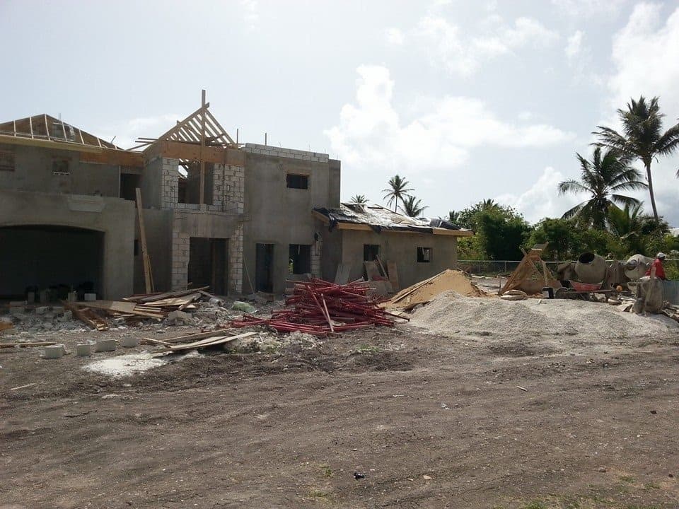 Two-storey residence at structural stage with roof framing beginning, scaffolding and cement mixer on site