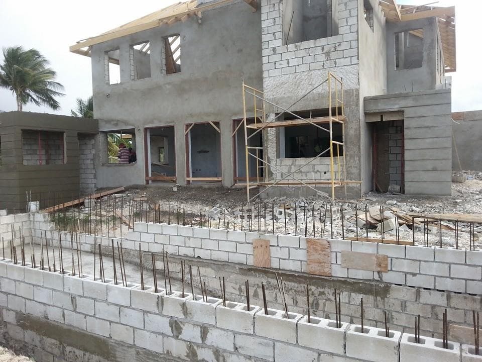 Two-storey residence with scaffolding erected and foundation walls with exposed rebar in foreground