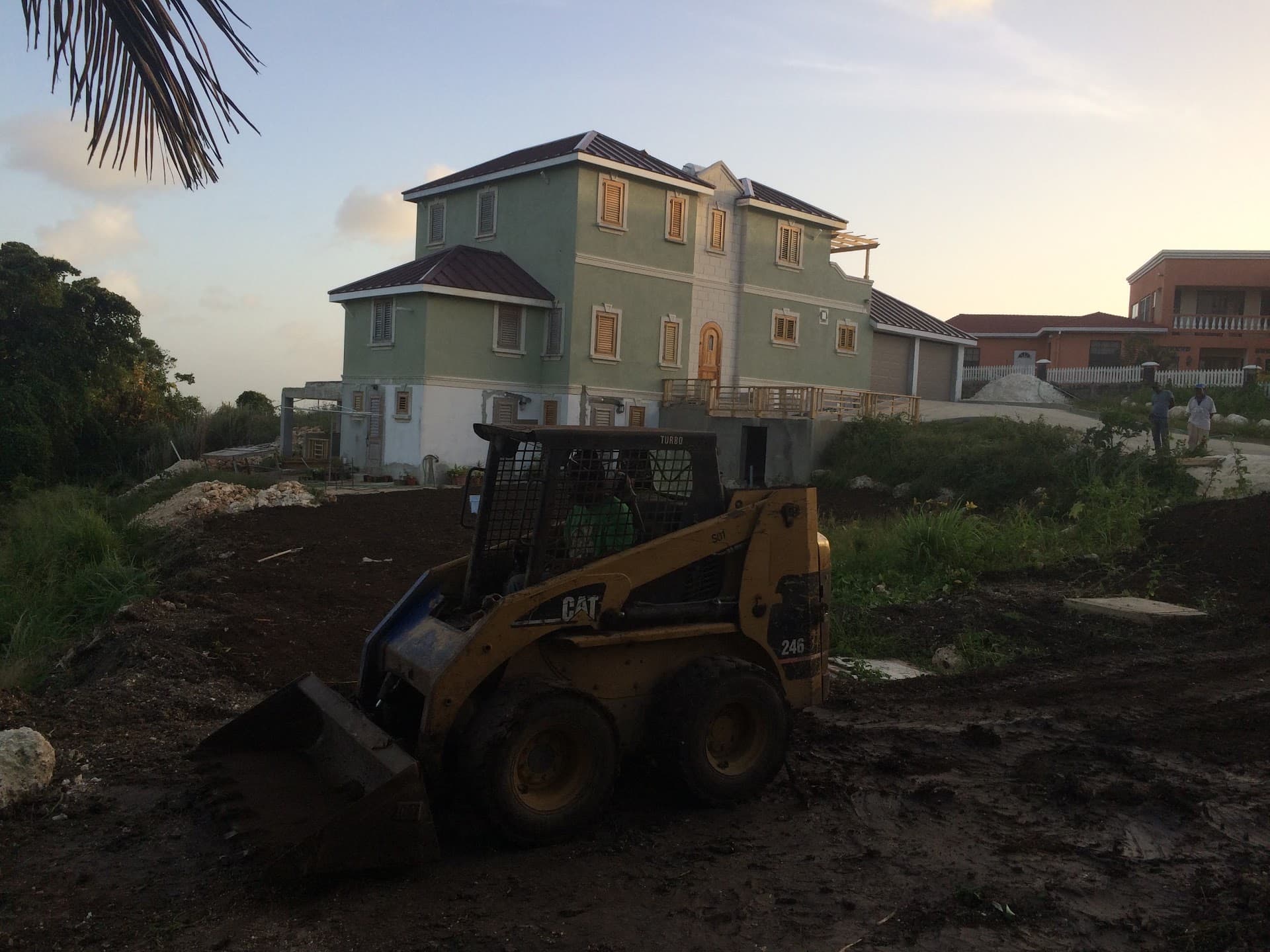 Three-storey green residence with skid-steer loader grading the site at dusk