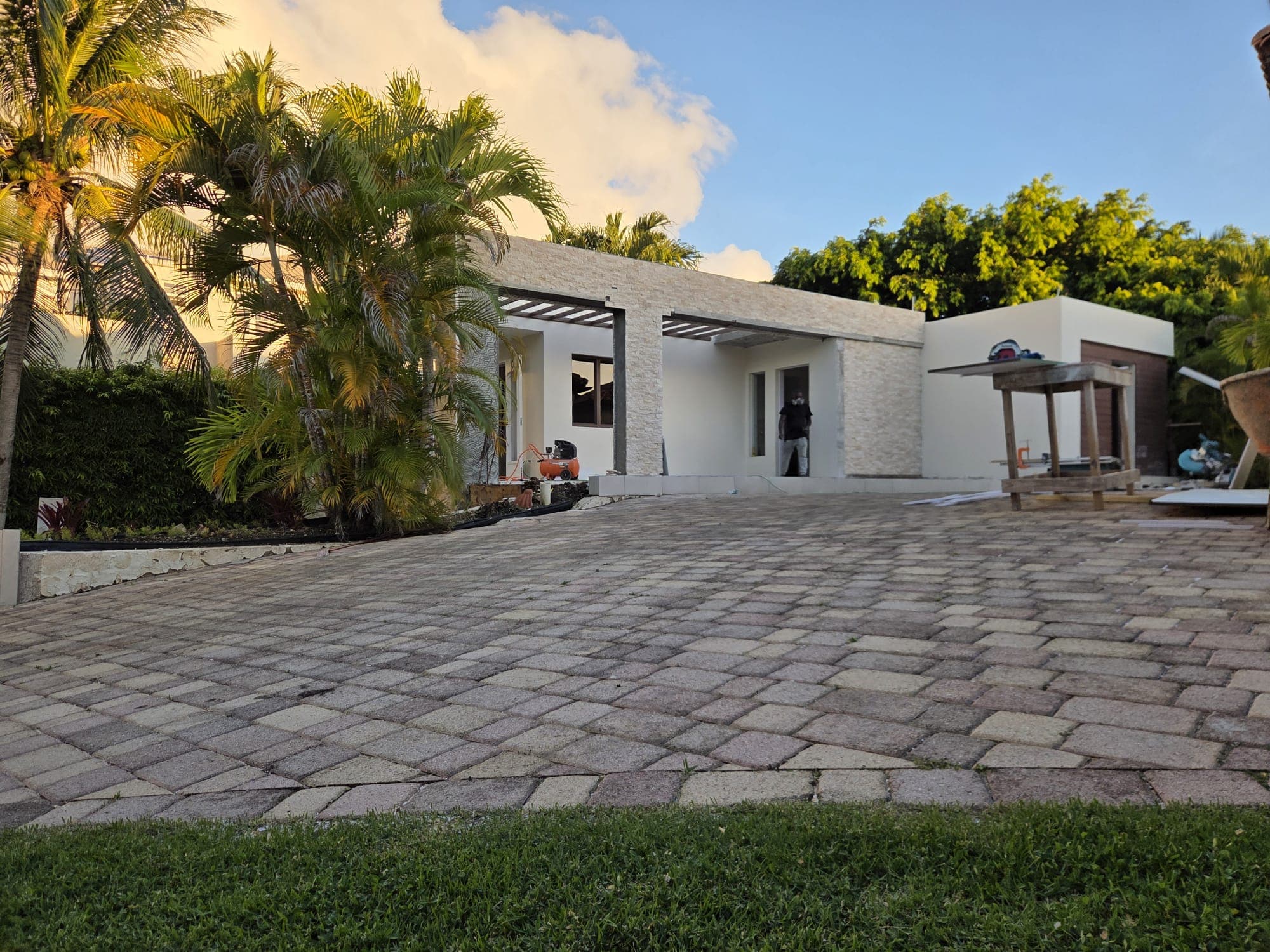 Single-storey new-build residence with stone cladding and pergola entry, under construction at dusk
