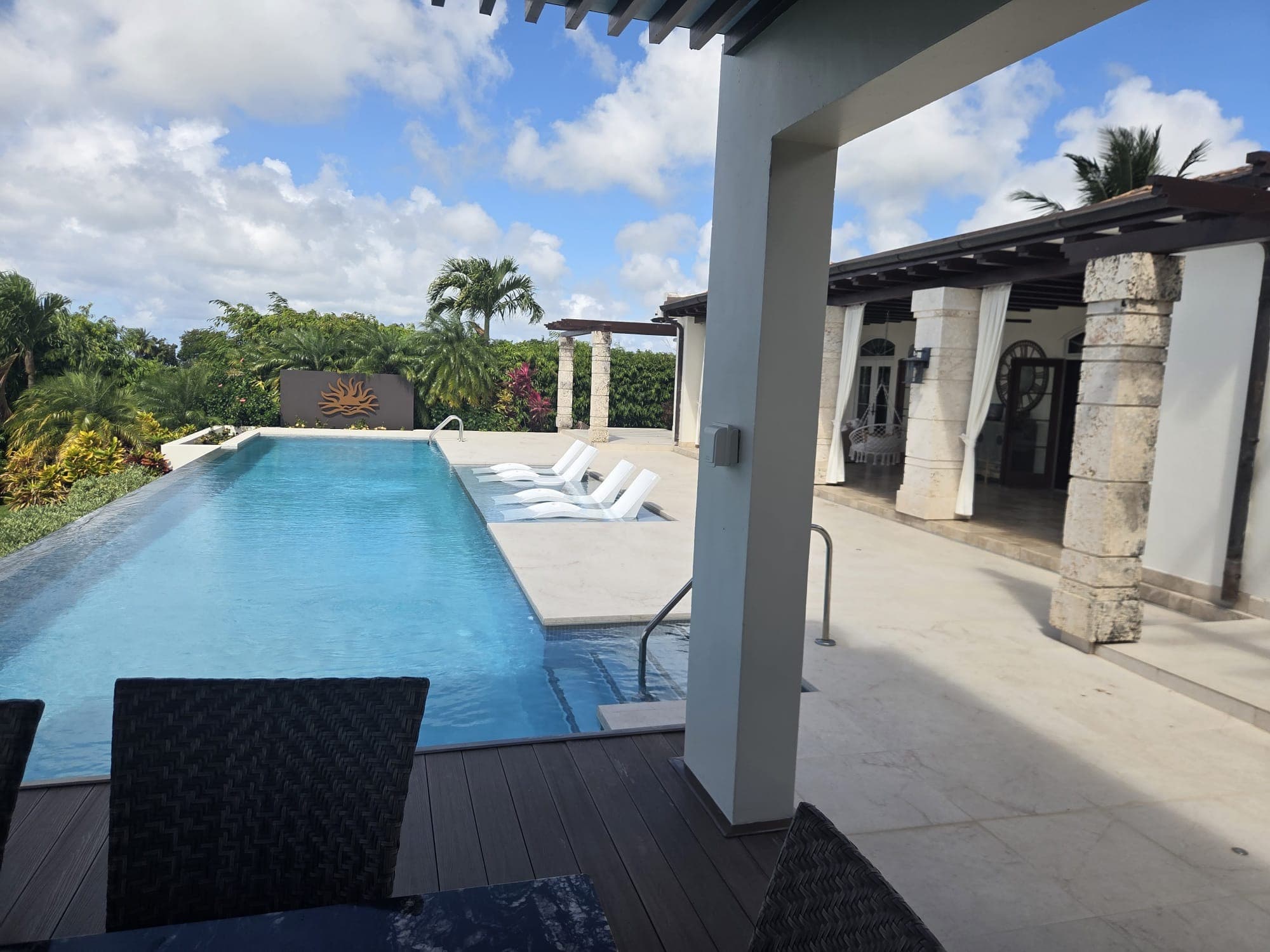 Infinity-edge pool terrace with a sun-motif water feature wall and covered lounge area