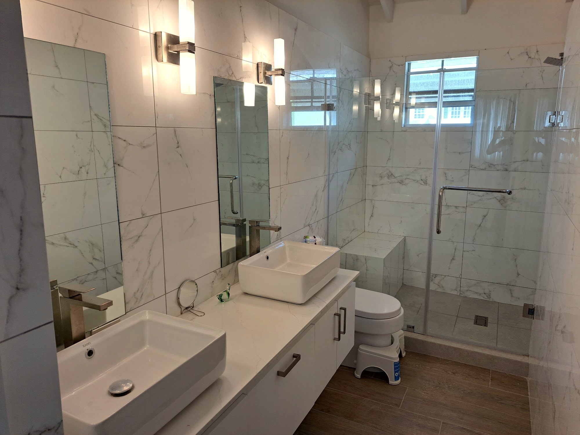 Renovated bathroom with double vanity, marble-tiled walls, and glass shower enclosure